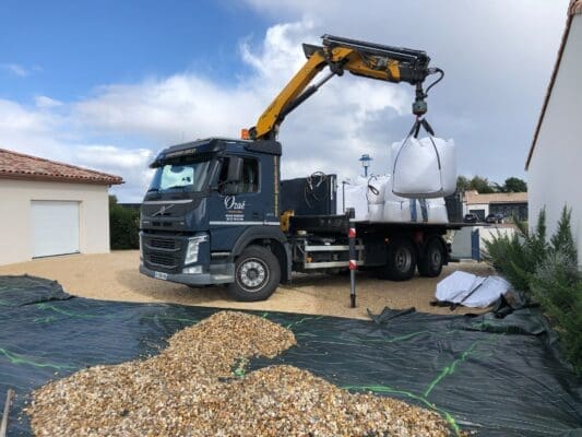 Camion Ozaé effectuant une livraison de graviers en big bag, avec bras de grue, pour l’aménagement d’une cour gravillonnée.